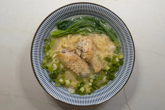 Creamy Tori Paitan chicken ramen in a cast iron Dutch oven topped with golden pan-fried chicken wings, crunchy Taiwanese A Choy, chopped green onions, and roasted sesame seeds using Nissin Demae Iccho 100% Hokkaido Wheat noodles.