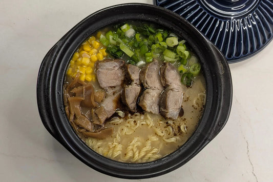Rich Black Garlic Oil Tonkotsu ramen served in a claypot, topped with tender char siu slices, sweet corn kernels, Japanese seasoned bamboo shoots (menma), and freshly chopped scallions using Nissin Demae Iccho 100% Hokkaido Wheat noodles.