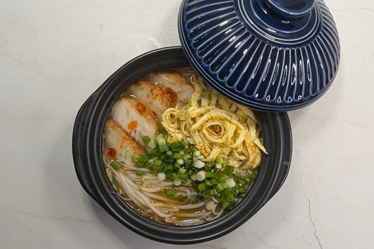 Takana Tonkotsu ramen in a bowl topped with sliced golden onion fish cakes, Kinshi Tamago egg ribbons, bean sprouts, green onions, toasted sesame seeds, and chili oil.