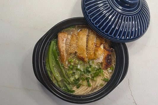 One-pot black garlic tonkotsu ramen in a bowl with crispy seared chicken thigh, flash-wilted A-choy, green onions, and black garlic oil