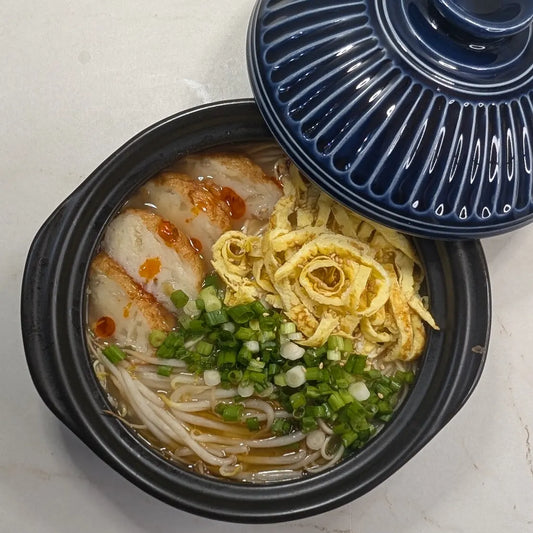 Takana Tonkotsu ramen in a bowl topped with sliced golden onion fish cakes, Kinshi Tamago egg ribbons, bean sprouts, green onions, toasted sesame seeds, and chili oil.